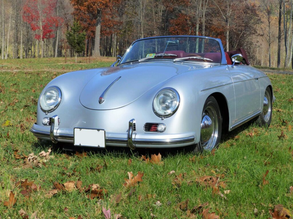 Silver 356 Roadster with red leather interior. Top is down and the vehicle sits in a grassy field